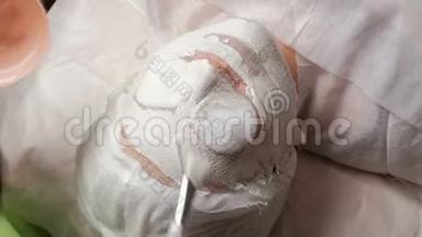 一个美容师或一个戴着白手套的<strong>整形外科</strong>医生用刷子把一个白色的石膏团涂在女孩脸上`纳罗